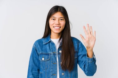 Genç Asyalı kadın gülümseyerek beş numarayı parmaklarıyla gösteriyor..