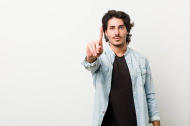 Beyaz arka planda genç yakışıklı bir adam parmaklarıyla bir numarayı gösteriyor..
