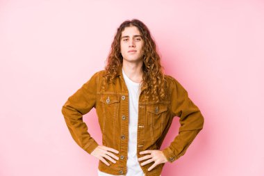 Genç, uzun saçlı, yalnız poz veren, kendine güvenen, ellerini kalçasında tutan adam..