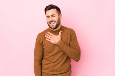 Pembe arka planda genç beyaz bir adam izole edilmiş kahkahalar atıyor ve elini göğsüne koyuyor..