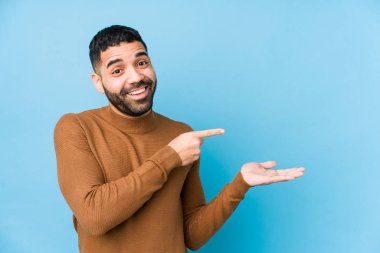 Mavi arka planda genç bir latin adam. Palmiye üzerinde bir kopya alanı tutarken heyecanlı..