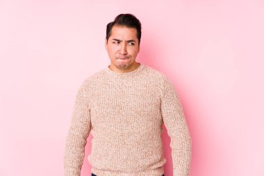 Pembe arka planda poz veren, kafası karışmış, kuşkulu ve güvensiz genç bir adam..