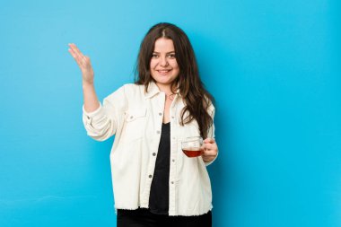 Genç, kıvrımlı bir kadın elinde çay fincanıyla hoş bir sürpriz yapıyor. Heyecanlı ve el kaldırıyor..