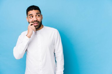 Mavi arka planda genç bir latin adam izole edilmiş, rahat bir şekilde fotokopi odasına bakan bir şeyi düşünüyor..