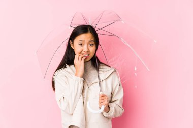 Şemsiye tutan genç Çinli kadın tırnaklarını yiyor, gergin ve endişeli..