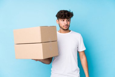 Genç Arap adam kutuları tek başına tutuyor. Kafası karışmış, kendinden emin değil..