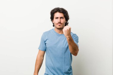 Beyaz arka planda kameraya yumruk sallayan genç yakışıklı bir adam, agresif yüz ifadesi..