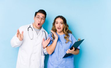 Mavi arka planda poz veren genç doktor çift şaşırdı ve şok oldu..