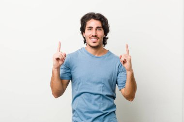 Beyaz bir arka planı olan genç yakışıklı bir adam iki elini de boş bir alan göstererek gösteriyor..