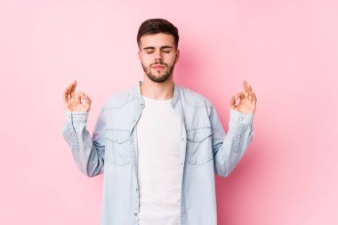 Beyaz arka planda poz veren beyaz tenli genç beyaz iş adamı sıkı çalışma gününden sonra dinleniyor, yoga yapıyor..