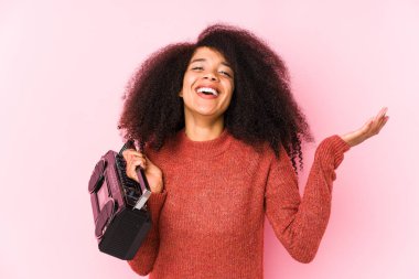 Elinde kaset tutan genç afro kadın hoş bir sürprizle karşılaşıyor, heyecanlı ve el kaldırıyor..