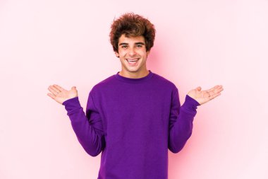Pembe arka planı olan genç beyaz bir adam kollarıyla ölçek oluşturuyor, mutlu ve kendinden emin hissediyor..