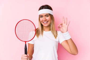 Badminton oynayan genç bir kadın neşeli ve kendinden emin bir şekilde iyi bir jest yapıyor..