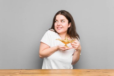 Kafkas kavisli genç bir kadın gri bir arka planda izole edilmiş sihirli bir lambaya arzu soruyor.