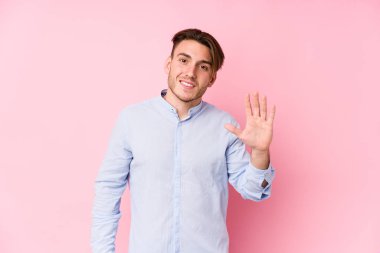 Pembe arka planda poz veren beyaz bir genç yalnız ve beş numarayı parmaklarıyla gülümsüyor..