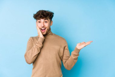 Genç Arap izole edilmiş bir adam, avuç içinde kopya alanı tutuyor, el ele yanak üzerinde tutuyor. Şaşırmış ve mutlu..