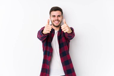 Beyaz arka planda poz veren beyaz tenli genç bir adam. Baş parmağıyla izole edilmiş. Bir konuda tezahürat yapıyor, destek ve saygı duyuyor..