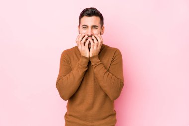 Pembe arka planda genç beyaz bir adam bir şeye gülüyor, elleri ile ağzını kapatıyor..