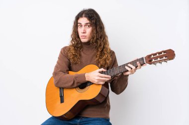 Gitar çalan beyaz bir genç omuz silkiyor ve gözleri açık..