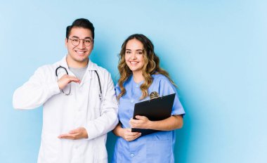 Mavi arka planda poz veren genç doktor çift iki elle bir şey tutuyor, ürün sunumu..