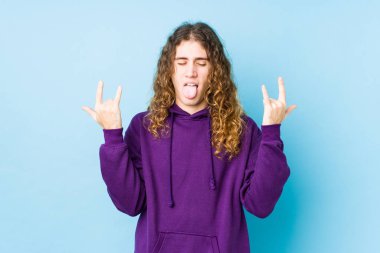 Uzun saçlı adam izole bir şekilde poz veriyor, parmaklarıyla kaya hareketi yapıyor.