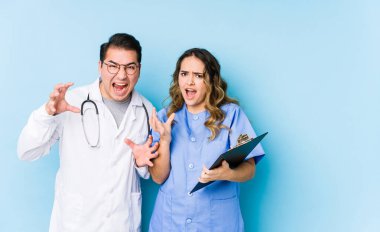 Mavi arka planda poz veren genç doktor çift öfkeyle bağırıyor..