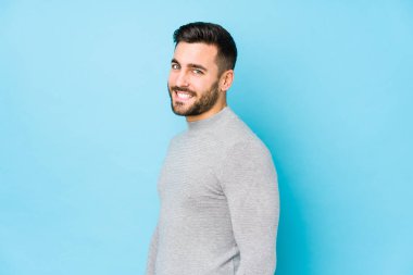 Mavi arka planda genç beyaz bir adam yalnız görünüyor. Gülümsüyor, neşeli ve keyifli..