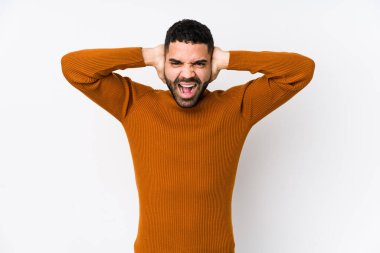 Genç Latin bir adam beyaz bir arkaplanda izole edilmiş kulakları kulaklarıyla kapatıyor çok fazla ses duymamaya çalışıyor..