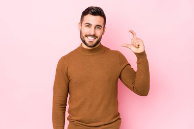 Pembe arka planda genç beyaz bir adam izole edilmiş, parmakları olan, gülümseyen ve kendinden emin bir şey tutuyor..
