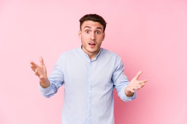 Pembe arka planda poz veren beyaz bir genç hoş bir sürprizle karşılaşıyor, heyecanlı ve el kaldırıyor..