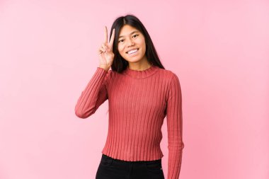 Genç Çinli kadın yalnız poz veriyor zafer işareti gösteriyor ve gülümsüyor..