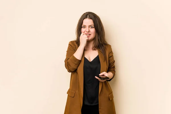 Young curvy woman holding a phone biting fingernails, nervous and very anxious.