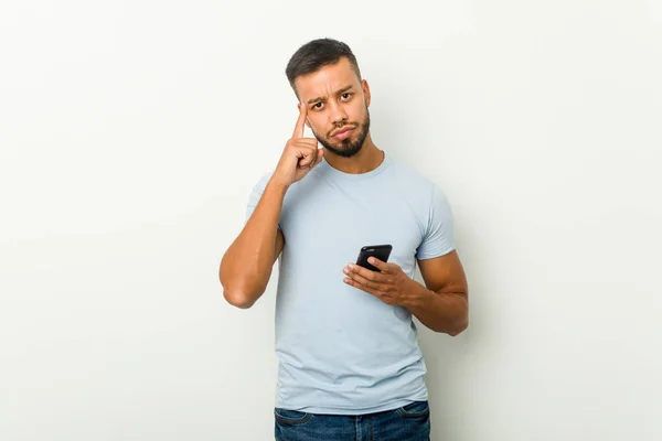 Joven Mestizo Asiático Hombre Sosteniendo Teléfono Apuntando Sien Con Dedo —  Fotos de Stock