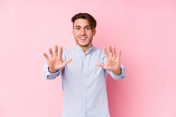 年轻的高加索男子 身披粉红的背景 与人隔离 手举十号 — 图库照片