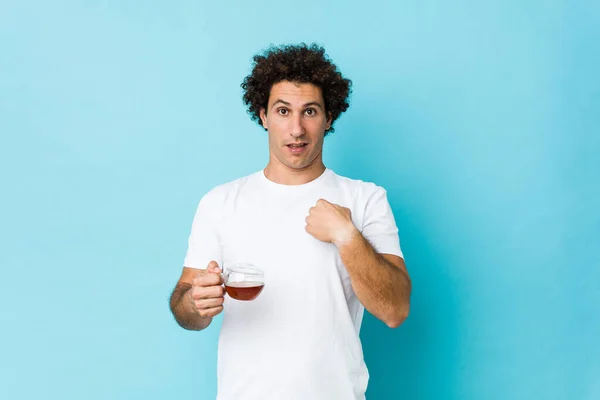 Jovem Homem Encaracolado Caucasiano Segurando Uma Xícara Chá Surpreso Apontando — Fotografia de Stock