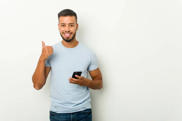 Joven Mixta Raza Asiático Hombre Sosteniendo Teléfono Sonriendo Levantando Pulgar —  Fotos de Stock