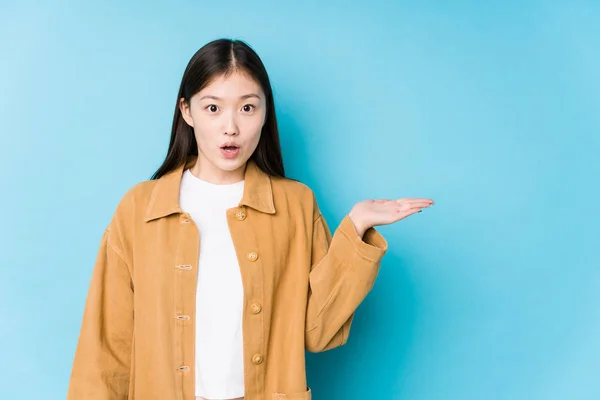 Joven Mujer China Posando Fondo Azul Aislado Impresionado Sosteniendo Espacio —  Fotos de Stock