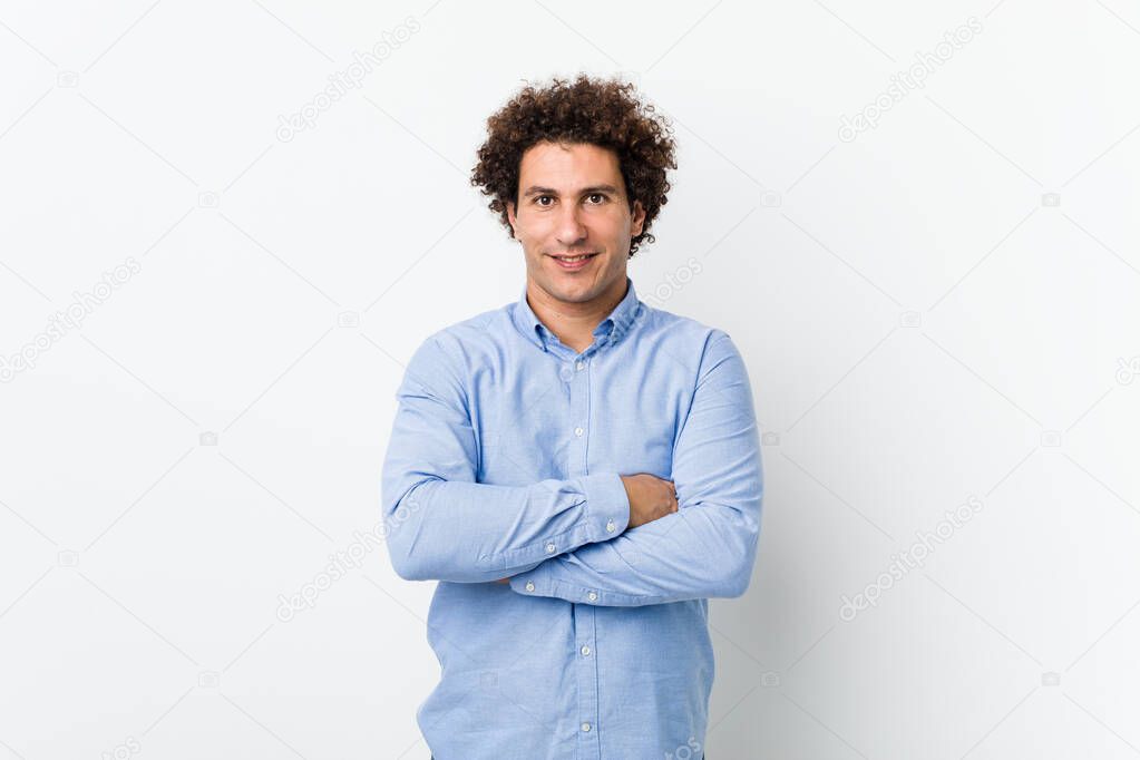 Young curly mature man wearing an elegant shirt who feels confident, crossing arms with determination.