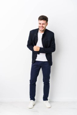 Tam vücut Kafkasyalı genç adam mutlu bir şekilde gülüyor ve ellerini karnının üstünde tutarak eğleniyor..