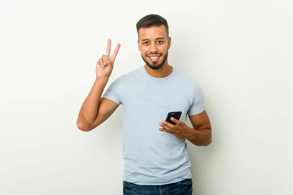 Jovem Mestiço Asiático Homem Segurando Telefone Mostrando Sinal Vitória Sorrindo — Fotografia de Stock