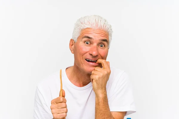 Homem Caucasiano Sênior Segurando Uma Escova Dentes Isolada Mordendo Unhas — Fotografia de Stock