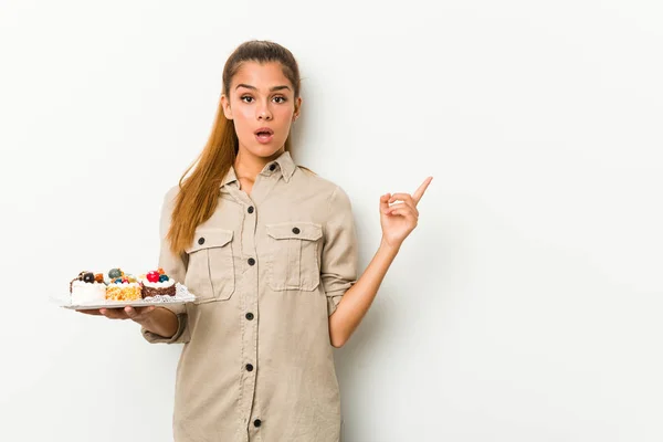 Young Caucasian Woman Holding Sweet Cakes Pointing Side — Stok fotoğraf