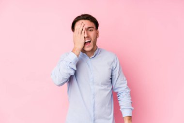 Pembe arka planda poz veren beyaz bir genç. Yüzünün yarısını palmiye ile kaplayarak eğleniyor..