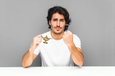 Kameraya yumruğunu gösteren sihirli bir lamba tutan genç adam, agresif yüz ifadesi..