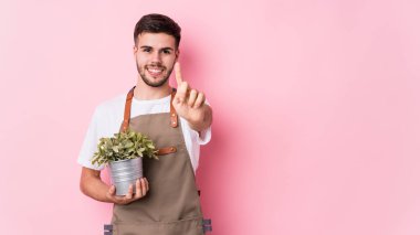 Kafkasyalı genç bahçıvan elinde bir bitki tutuyor. Bir numarayı parmağıyla gösteriyor..