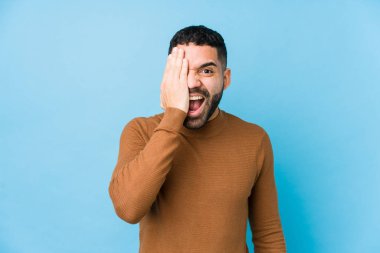 Mavi bir geçmişi olan genç bir latin adam yüzünün yarısını avuç içiyle kaplayarak eğleniyor..