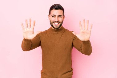 Pembe arka planda genç beyaz bir adam 10 numarayı elleriyle gösteriyor..