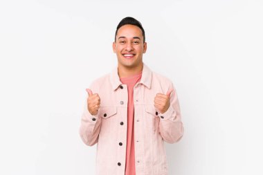 Genç Latin adam yalnız poz veriyor. İki parmağını da kaldırıyor, gülümsüyor ve kendinden emin..