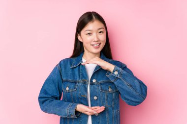 Pembe arka planda poz veren genç Çinli kadın iki eliyle bir şey tutuyor, ürün sunumu..