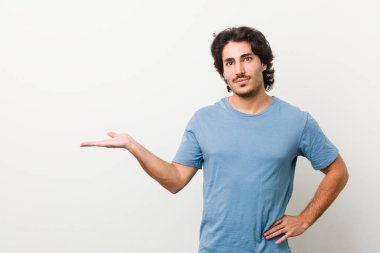 Beyaz arka planda genç yakışıklı bir adam bir avuç içinin fotokopisini çekiyor ve başka bir eli belinde tutuyor..